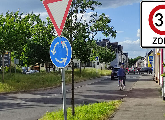 Ein Foto des Kreisverkehrs bei ALDI auf der Gerresheimer Straße. Ein Tempo 30-Zone Zeichen ist überlagert.