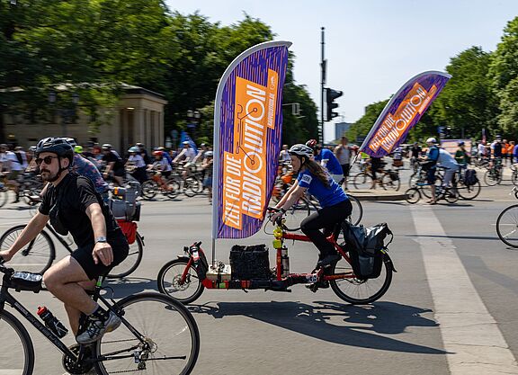 Viele Menschen auf Fahrrädern. An einem Rad befindet sich eine große Fahne mit dem Wort "Radvolution" darauf.