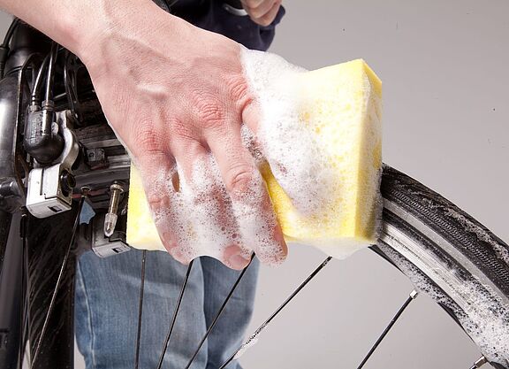 Pflege Großaufnahme einer Hand mit Schwamm und Schaum, die ein Fahrrad-Vorderrad säubert.